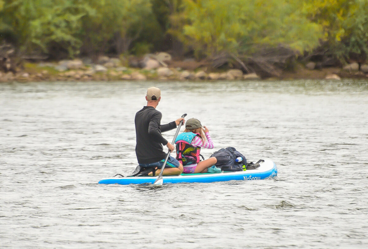 A father and daughter on a stand-up-paddleboard floating down a river