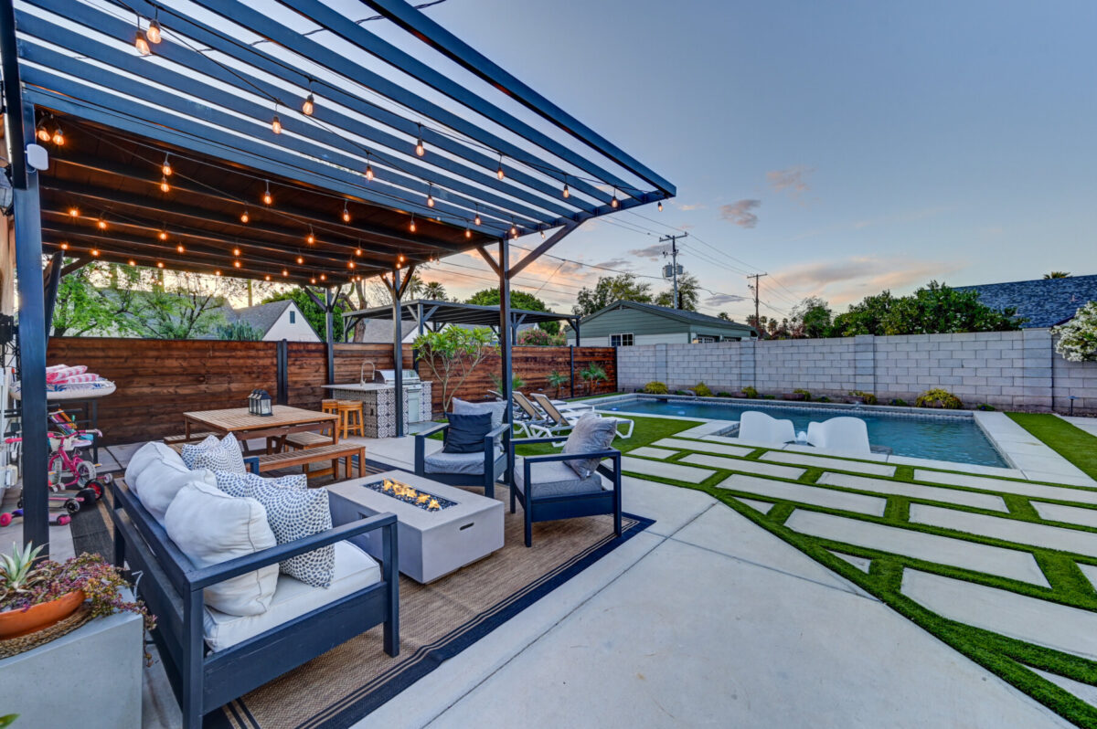 Luxury Scottsdale vacation rental backyard with private pool, covered pergola, string lights, fire pit seating area, and artificial turf at dusk