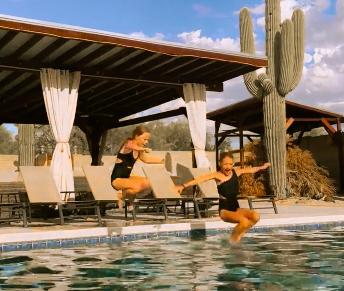 Two children jumping into a private pool at a Scottsdale vacation rental with a covered cabana, lounge chairs, and saguaro cactus in the background