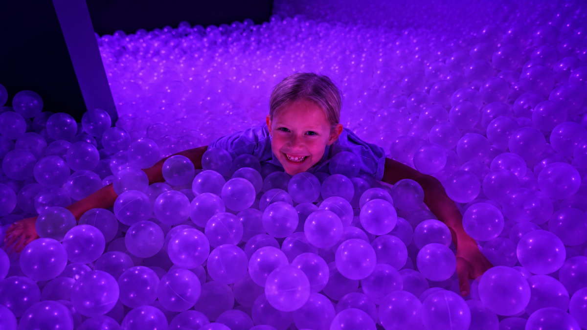 Child smiling in the purple-lit Bubble Bath Pit at Bubble Planet Phoenix in Tempe, Arizona